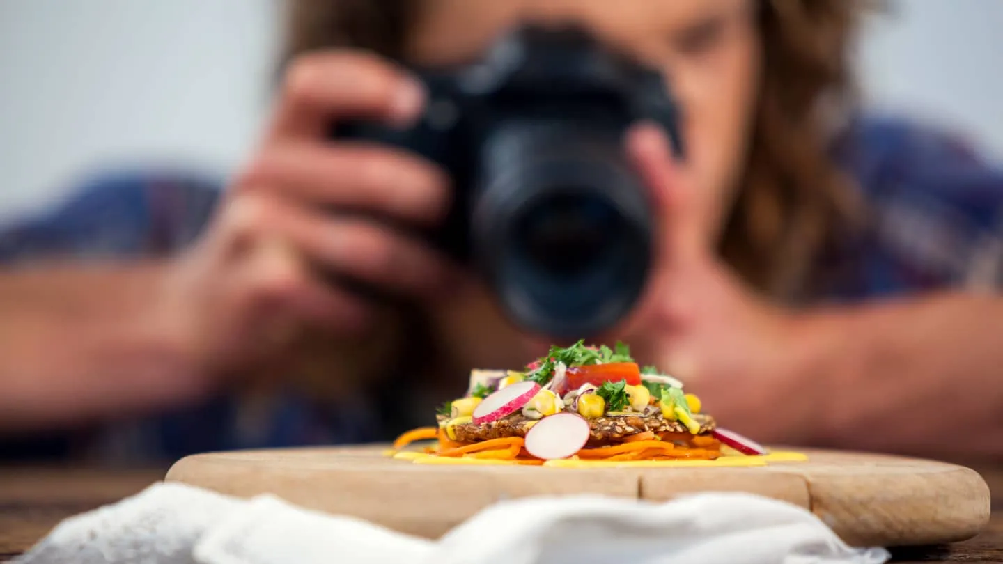 A photographer leaning close over a plated dish, camera raised — the scroll moves smoothly into the lens